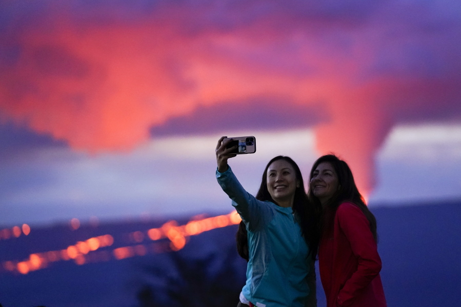 Ingrid Yang, left, and Kelly Bruno, both of San Diego, take a photo in front of lava erupting from Hawaii's Mauna Loa volcano Wednesday, Nov. 30, 2022, near Hilo, Hawaii.