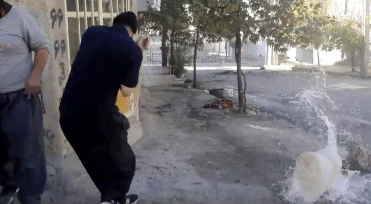 In this image from video provided by Hengaw Organization for Human Rights, a protester reacts after a water container was hit by a bullet during a protest in Javanroud, a Kurdish town in western Iran, Monday, Nov. 21, 2022.