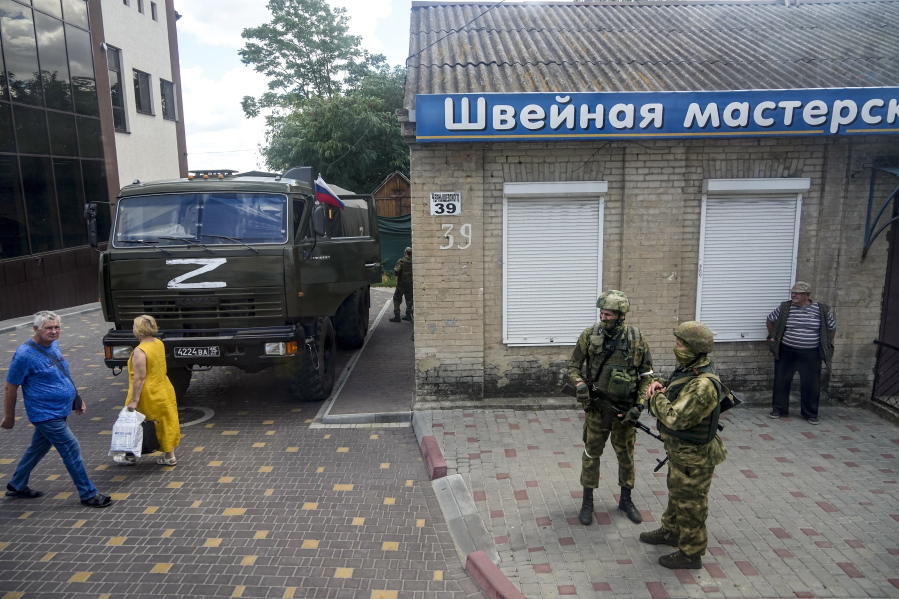 FILE - Russian soldiers guard an office for Russian citizenship applications as their military truck is parked nearby, in Melitopol, south Ukraine, on July 14, 2022. As Russians seized parts of eastern and southern Ukraine in the 8-month-old war, mayors, civilian administrators and others, including nuclear power plant workers, say they have been abducted, threatened or beaten to force their cooperation. In some instances, they have been killed. Human rights activists say these actions could constitute a war crime.