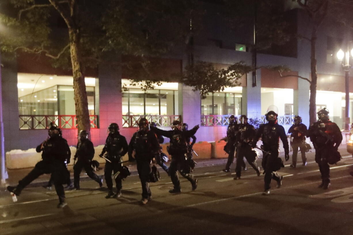 FILE - Portland police chase demonstrators during a Black Lives Matter protest on July 26, 2020, in Portland, Ore. The city of Portland, Oregon, has settled a federal lawsuit over its police bureau's use of tear gas and other crowd control devices during racial justice protests in 2020.