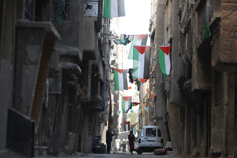 File - People walk under Palestinian flags in Yarmouk camp in Damascus Syria that has seen heavy fighting during the civil war, Wednesday, Nov. 2, 2022. A trickle of residents has returned to Yarmouk, the large Palestinian refugee camp-turned-Damascus neighborhood that was devastated in the country's civil war.