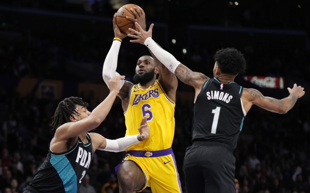 Los Angeles Lakers forward LeBron James, center, shoots as Portland Trail Blazers forward Trendon Watford, left, and guard Anfernee Simons defends during the first half of an NBA basketball game Wednesday, Nov. 30, 2022, in Los Angeles. (AP Photo/Mark J.