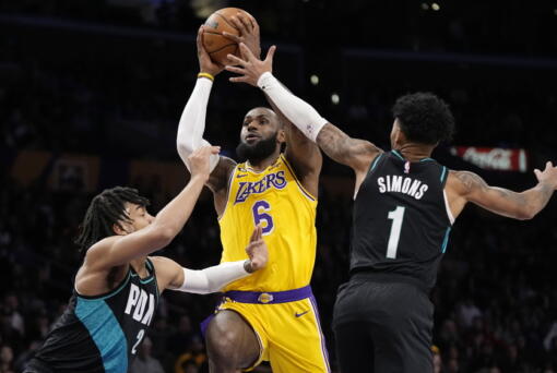Los Angeles Lakers forward LeBron James, center, shoots as Portland Trail Blazers forward Trendon Watford, left, and guard Anfernee Simons defends during the first half of an NBA basketball game Wednesday, Nov. 30, 2022, in Los Angeles. (AP Photo/Mark J.
