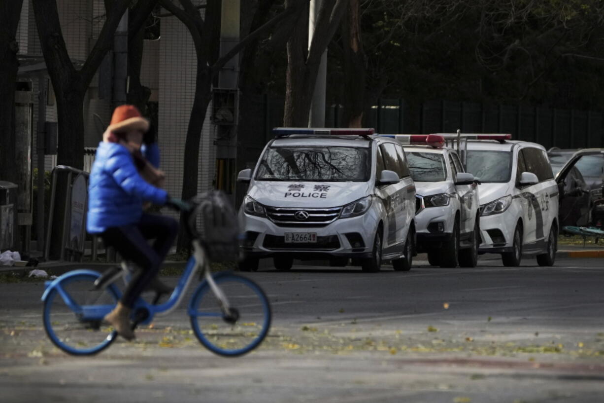 A woman rides past police vehicles parked along a road monitoring near the site of last weekend protest in Beijing, Tuesday, Nov. 29, 2022. With police out in force, there was no word of protests Tuesday in Beijing, Shanghai or other major cities.