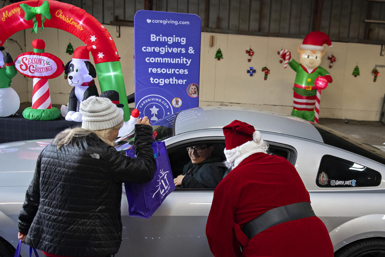 Debbie Russell, left, one of the founders of the annual Caregiver Christmas, greets Asdrual Garcia, son of a caregiver, as he picks up a gift package on her behalf while joined by Santa, also known as Ralph Heiser.
