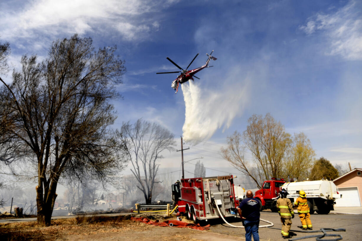 A Sikorsky helicopter makes a water drop on homes that burned along Acequia Drive on April 20, 2022, in Monte Vista, Colorado. The threat of more fires is increasing in recent days due to the high temperatures. (Helen H.