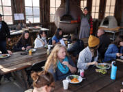 Classmates sit and eat Pasta al Forno, an Italian dish made by Robin Morgan, a PhD student at the Bread Lab, and two types of salad during the Pizza for Producers Training at the WSU Bread Lab in Burlington, Washington, on Oct. 28, 2022. The pasta dish was made in a wood-fired oven converted from a World War II Anti-Submarine Net Buoy seen in the back.