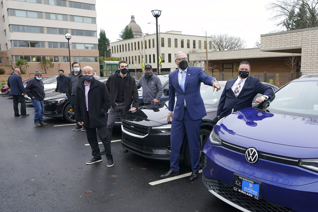 Washington Gov. Jay Inslee, second from right, poses for a photo, Monday, Dec. 13, 2021, with car dealership representatives who drive electric vehicles to a news conference in Olympia, Wash. Inslee announced several climate-related proposals for the 2022 legislative session, including a plan to offer rebates on the purchase of new and used electric vehicles for qualified buyers. (AP Photo/Ted S.