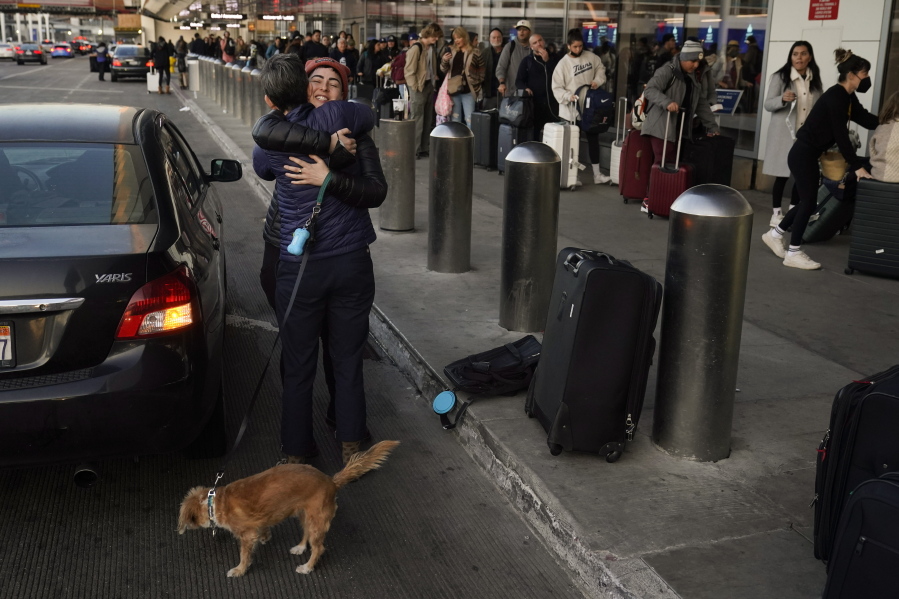 Two people hug outside a terminal as travelers wait in line to check in at Los Angeles International Airport in Los Angeles, Monday, Dec. 19, 2022. (AP Photo/Jae C.