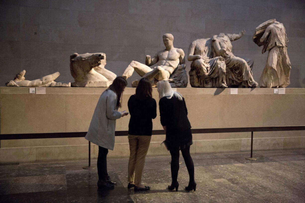 FILE - Women stand by a marble statue of a naked youth thought to represent Greek god Dionysos, center, from the east pediment of the Parthenon, on display during a media photo opportunity to promote a forthcoming exhibition on the human body in ancient Greek art at the British Museum in London, Thursday, Jan. 8, 2015. The British Museum has pledged not to dismantle its collection following a report that the institution's chairman has held secret talks with Greece's prime minister over the return of the Parthenon Sculptures, also known as the Elgin Marbles.