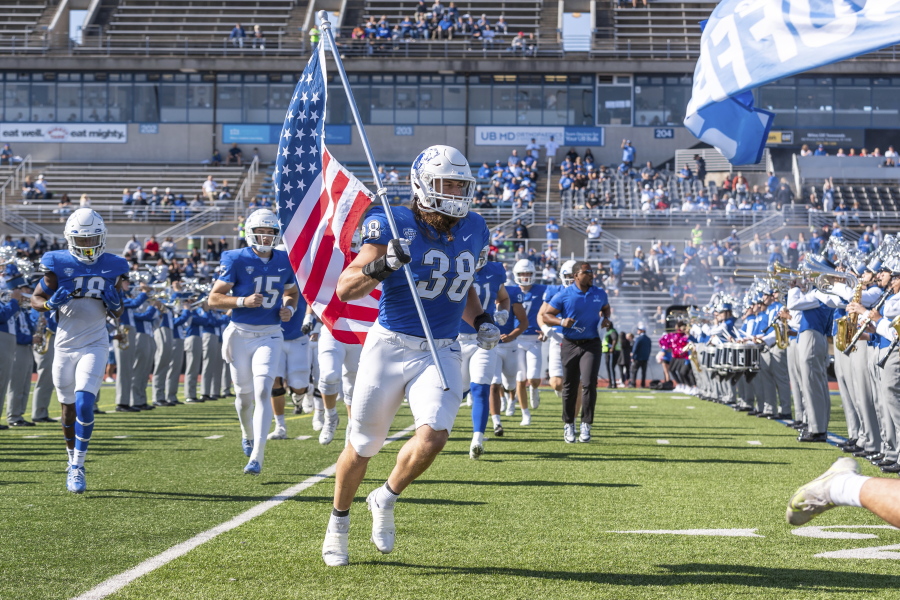 This Oct. 22, 2022, photo provided by University of Buffalo Athletics shows University at Buffalo NCAA college football player Damian Jackson (38) carrying the American flag as the team takes the field before a game against Toledo, in Buffalo, N.Y. Jackson has no expectation of growing emotional in preparing to play the final game of his college career next week.  (Paul Hokanson/Univ.