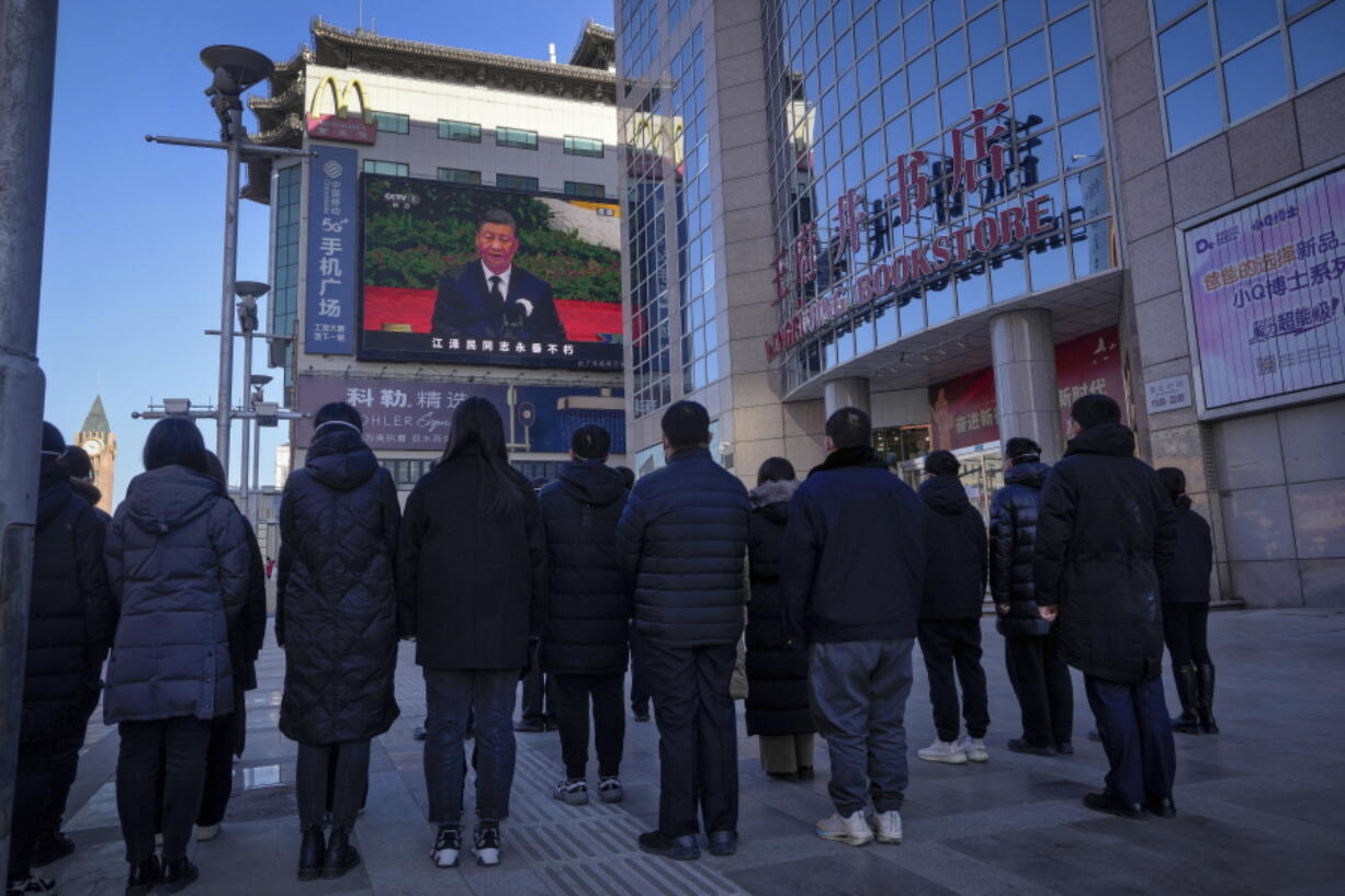 People watch a live broadcast of the memorial service for late former Chinese President Jiang Zemin where Chinese President Xi Jinping makes a speech on screen at the Wangfujing shopping street in Beijing, Tuesday, Dec. 6, 2022. A formal memorial service was held Tuesday at the Great Hall of the People, the seat of the ceremonial legislature in the center of Beijing.