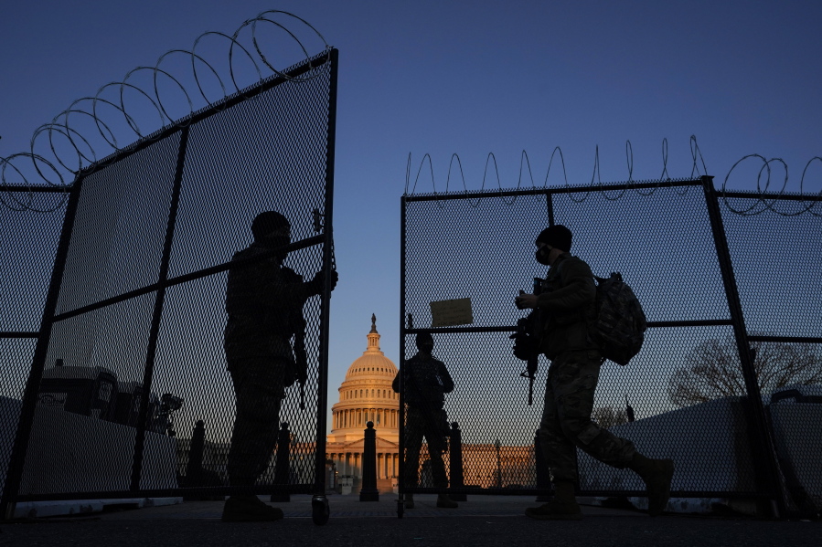 FILE - National Guard soldiers open a gate of the razor wire-topped perimeter fence around the Capitol to allow a colleague in at sunrise in Washington, March 8, 2021.