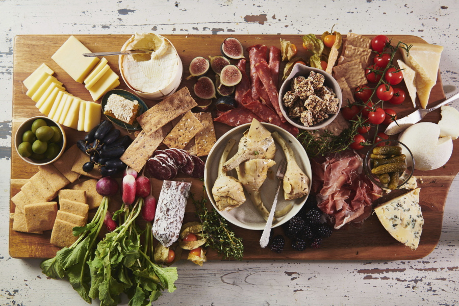 A variety of cheeses, spreads and cured meats are displayed on a graze board. Olives, pickles, and marinated vegetables of all kinds offer a tangy crunch and briney flavor in between bites of cheeses and charcuterie.