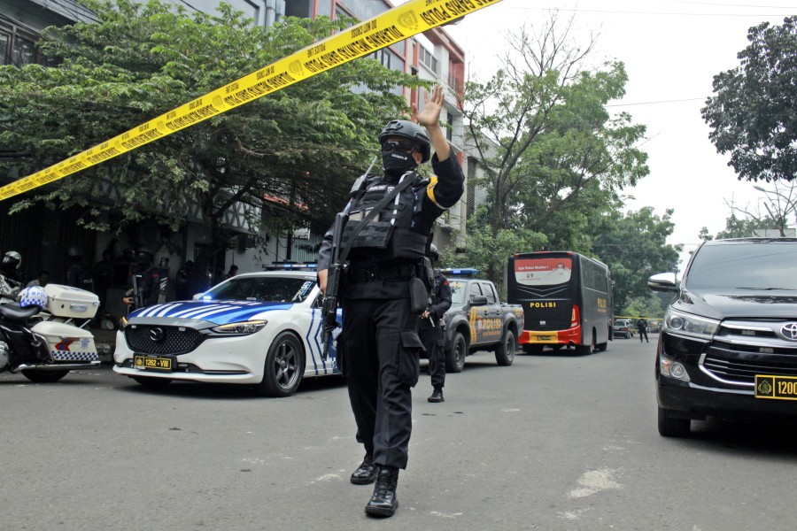 A police officer gestures at the crowd to move back as he guards a road leading to a police station where a bomb exploded in Bandung, West Java, Indonesia, Wednesday, Dec. 7, 2022. A man blew himself up Wednesday at a police station on Indonesia's main island of Java in what appeared to be the latest in a string of suicide attacks in the world's most populous Muslim nation.