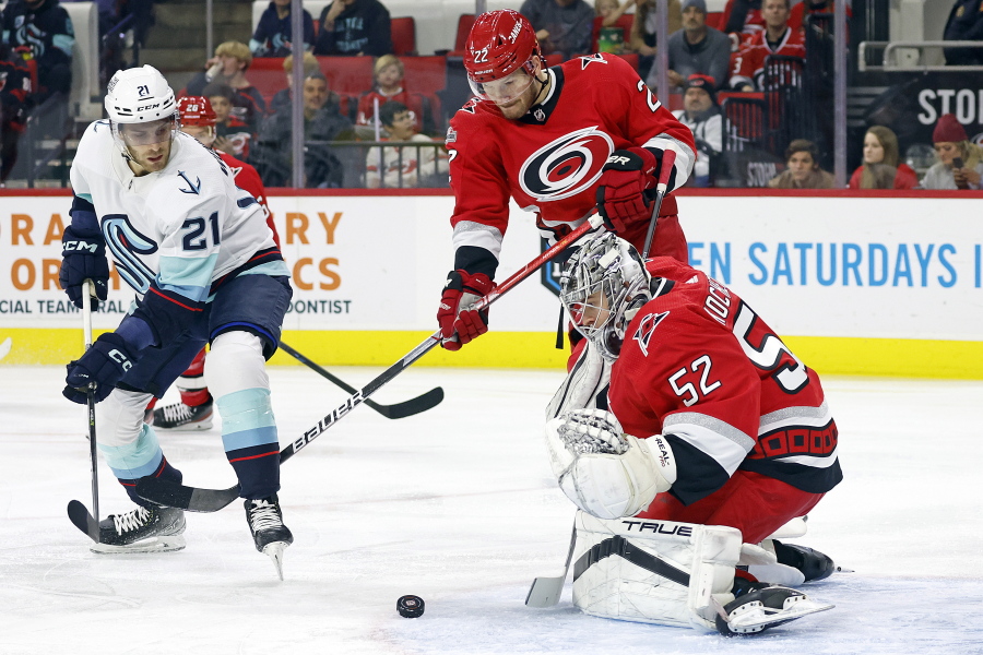 Seattle Kraken's Alex Wennberg (21) watches Carolina Hurricanes goaltender Pyotr Kochetkov (52) play the puck with Hurricanes' Brett Pesce (22) nearby during the first period of an NHL hockey game in Raleigh, N.C., Thursday, Dec. 15, 2022.