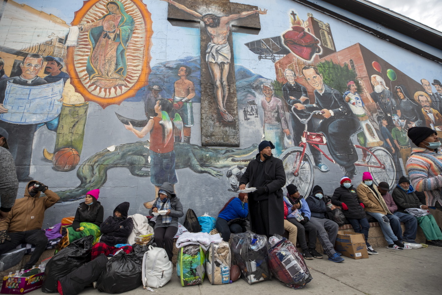 Migrants eat and wait for help while camping on a street in downtown El Paso, Texas, Sunday, Dec. 18, 2022. Texas border cities were preparing Sunday for a surge of as many as 5,000 new migrants a day across the U.S.-Mexico border as pandemic-era immigration restrictions expire this week, setting in motion plans for providing emergency housing, food and other essentials.