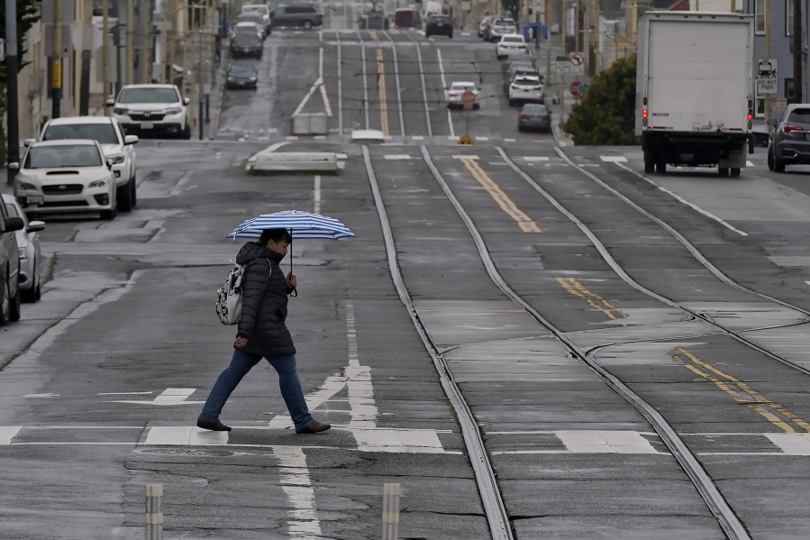 FILE - A pedestrian carries an umbrella while crossing a street in San Francisco, Thursday, April 14, 2022.  A variety of new laws take effect Sunday, Jan. 1, 2023 that could have an impact on people's finances and, in some cases, their personal liberties.