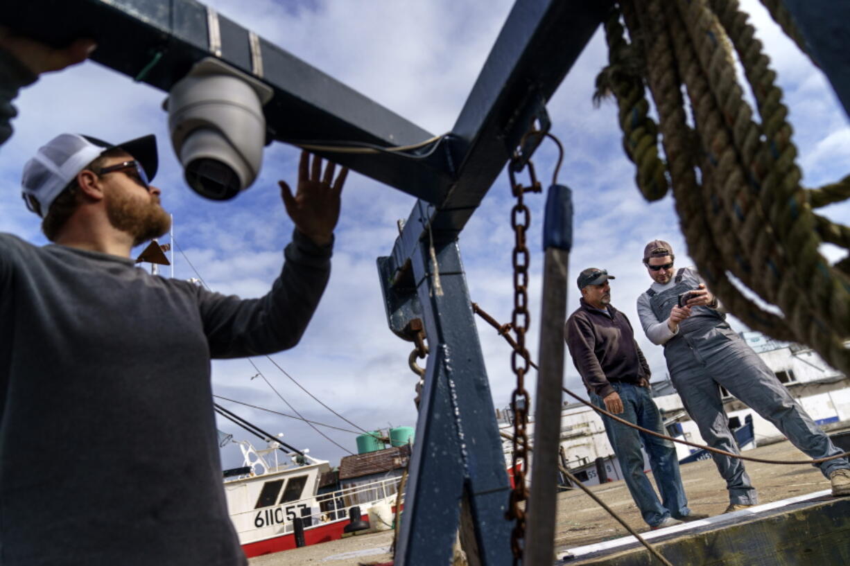 Mark Hager, left, positions a camera with the help of Anthony Lucia, right, as captain Al Cottone watches the feed on a monitor from his boat, the Sabrina Maria, in Gloucester, Mass., May 11, 2022. Hager's Maine-based startup, New England Maritime Monitoring, is one of a bevy of companies seeking to help commercial vessels comply with new federal mandates aimed at protecting dwindling fish stocks. But taking the technology overseas, where the vast majority of seafood consumed in the U.S. is caught, is a steep challenge.