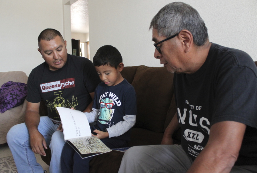 Micca Madalena, center, reads to his father, Darryl Madalena, left, and grandfather Myron Ami in his native language of Towa after getting home from school at Jemez Pueblo, N.M., Oct. 7, 2022. Darryl Madalena is advocating for more Native Americans to consider joining the organ donation rolls.