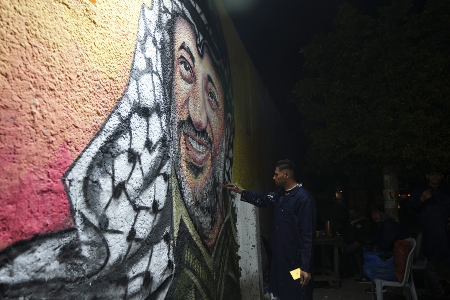 A Palestinian artist paints a portrait of of the late Palestinian president Yasser Arafat, on a wall in preparation of celebration of 58th Fatah anniversary, at the main square in Gaza City, Friday, Dec. 30, 2022.