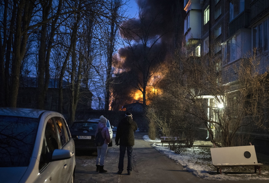 Residents watch at a burning infrastructure project hit during a massive Russian drone night strike in Kyiv, Ukraine, Monday, Dec. 19, 2022.