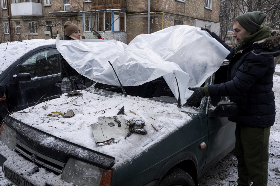 A couple cover their damaged car with a plastic tarp after a Russian attack in Kyiv, Ukraine, Wednesday, Dec. 14, 2022.