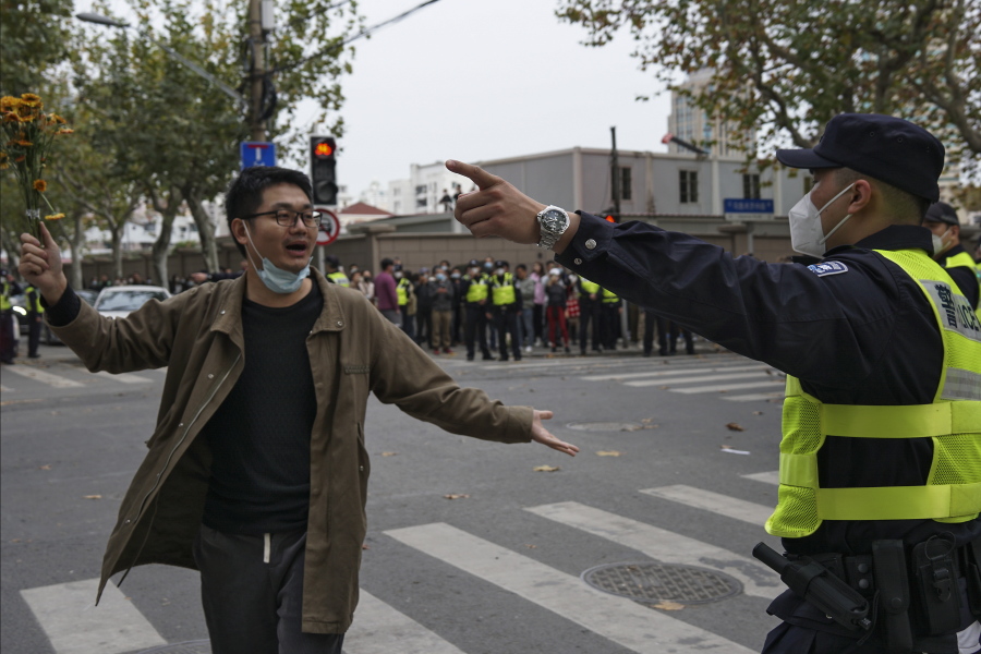 FILE - A protester holding flowers is confronted by a policeman during a protest on a street in Shanghai, China on Nov. 27, 2022. What started as an unplanned vigil last weekend in Shanghai by fewer than a dozen people grew hours later into a rowdy crowd of hundreds. The protesters expressed anger over China's harsh COVID-19 policies that they believed played a role in the deadly fire on Nov. 24 in a city in the far west.