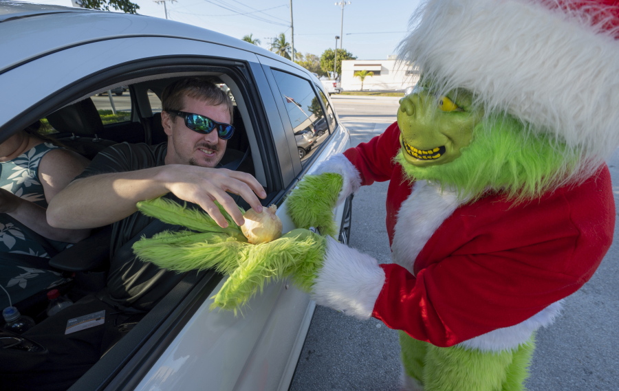 In this photo provided by the Florida Keys News Bureau, a Maryland motorist, left, accepts an onion instead of a traffic citation from Monroe County Sheriff's Office Colonel Lou Caputo, right, costumed as the Grinch, Tuesday, Dec. 13, 2022, in Marathon, Fla. For drivers slightly speeding through a school zone on the Florida Keys Overseas Highway Tuesday, Caputo offered them the choice between an onion or a traffic citation. It's a holiday tradition in the Keys that Caputo began 20 years ago to educate drivers that Keys schools remain in session through Dec. 16.