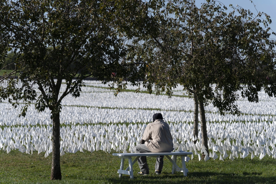 FILE - A visitor sits on a bench to look artist Suzanne Brennan Firstenberg's "In America: Remember," a temporary art installation made up of white flags to commemorate Americans who have died of COVID-19, on the National Mall in Washington on Oct. 2, 2021. The number of U.S. deaths has dropped in 2022 after soaring for two years during the COVID-19 pandemic, but it still is much higher than the levels before the coronavirus hit.