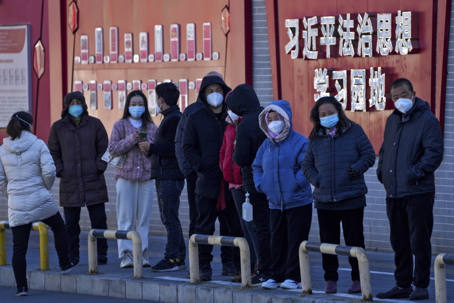 Residents wearing face masks line up for their routine COVID-19 tests along a wall displaying the words "Xi Jinping rule of law ideology learning ground" in Beijing, Monday, Dec. 5, 2022. China is easing some of the world's most stringent anti-virus controls and authorities say new variants are weaker. But they have yet to say when they might end a "zero-COVID" strategy that confines millions of people to their homes and set off protests and demands for President Xi Jinping to resign.