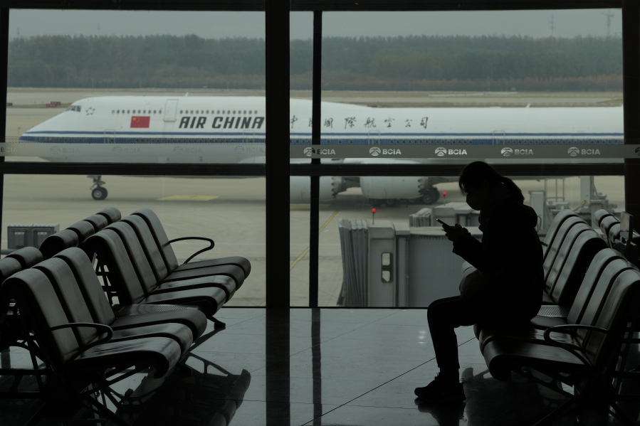 A passenger checks her phone as an Air China passenger jet taxi past at the Beijing Capital International airport in Beijing, Saturday, Oct. 29, 2022. China will drop a COVID-19 quarantine requirement for passengers arriving from abroad starting Jan. 8. The National Health Commission announced the change Monday, Dec. 26, 2022 as part of the latest easing of China's once strict virus control measures.