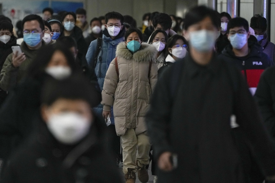 FILE - Masked commuters walk through a walkway in between two subway stations as they head to work during the morning rush hour in Beijing, Tuesday, Dec. 20, 2022. China continues to adapt to an easing of strict virus containment regulations. About three years ago, the original version of the coronavirus spread from China to the rest of the world and was eventually replaced by the delta variant, then omicron and its descendants, which continue plaguing the world today.