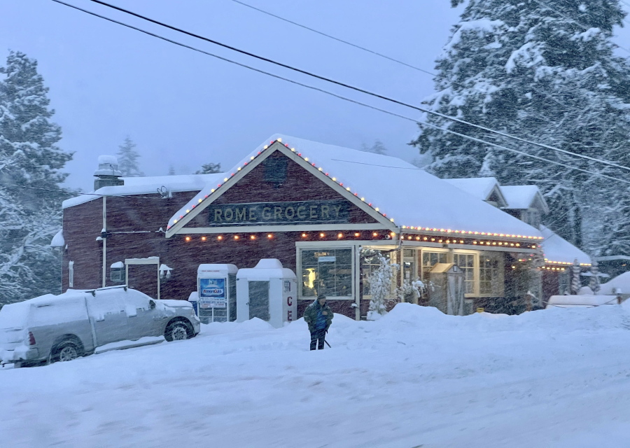 A person shovels snow outside Rome Grocery northeast of Bellingham, Wash., on Tuesday morning, Dec. 20, 2022. Heavy snow, freezing rain and sleet have disrupted travel across the Pacific Northwest, causing widespread flight cancellations and creating hazardous driving conditions.