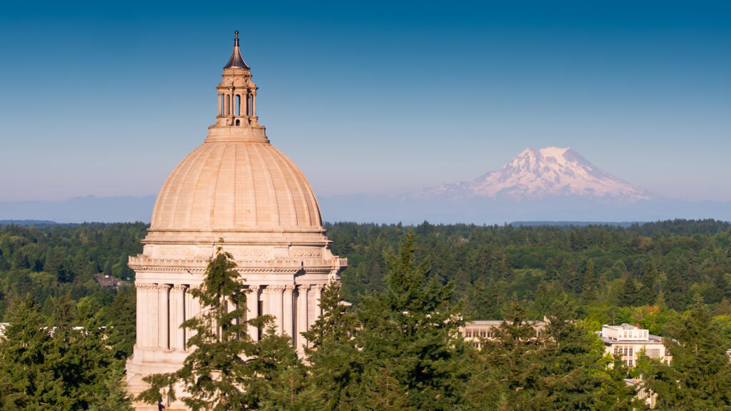 Aerial shot of the state capitol building in Olympia, Washington on a summer afternoon, with the snowy mass of Mt Rainier/Tahoma in the distance.