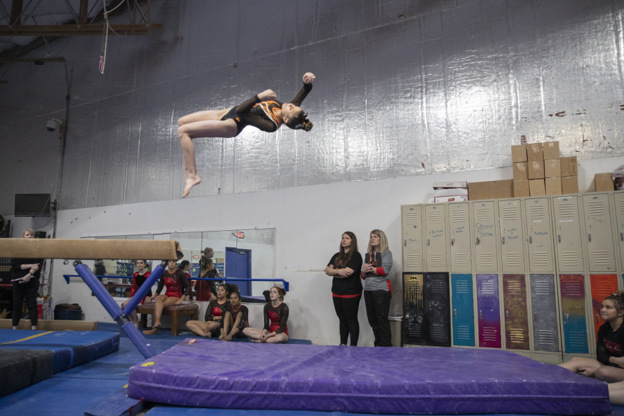 Reese Velansky of Washougal High School dismounts from the balance beam as Camas coaches and gymnasts look on during a meet at Naydenov Gymnastics on Dec. 17.