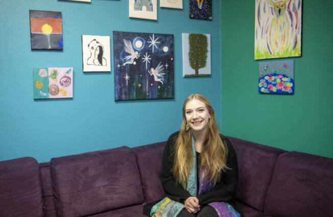 Youth House staff member Maranda Heckler sits for a portrait below artwork created by clients who are part of the Options or Healthy Transitions programs at Clark County Youth House. Heckler is a case manager and a certified peer counselor with the Healthy Transitions Program, where she uses her own lived experience to offer support to youth struggling with their mental health.