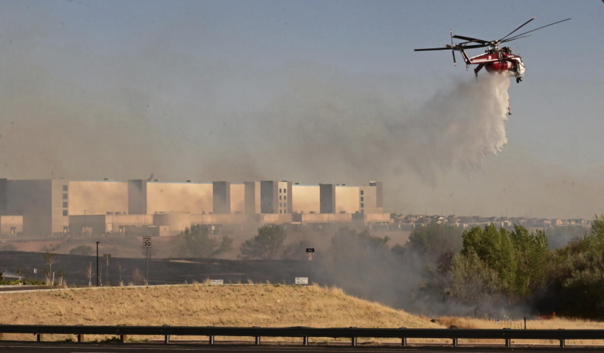 FILE - A helicopter drops water on flames from the Alturas Fire across Powers Blvd. from the Amazon Distribution Center on Thursday, May 12, 2022.  A bill introduced in the Colorado legislature would create a $2 million pilot program to use cameras, likely with AI technology, in high-risk locations to help identify fires before they burn out of control.