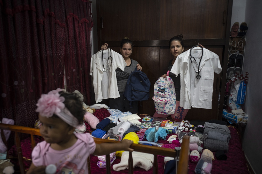 Melanie Rolo Gonzalez, right, and her sister Merlyn, pose for a photo with their medical student uniforms as they pack supplies for their journey to the U.S., in their home in Havana, Cuba, Saturday, Dec. 10, 2022. The sisters' voyage is one that hundreds of thousands of Cubans have made over the last two years in a historic wave of migration.