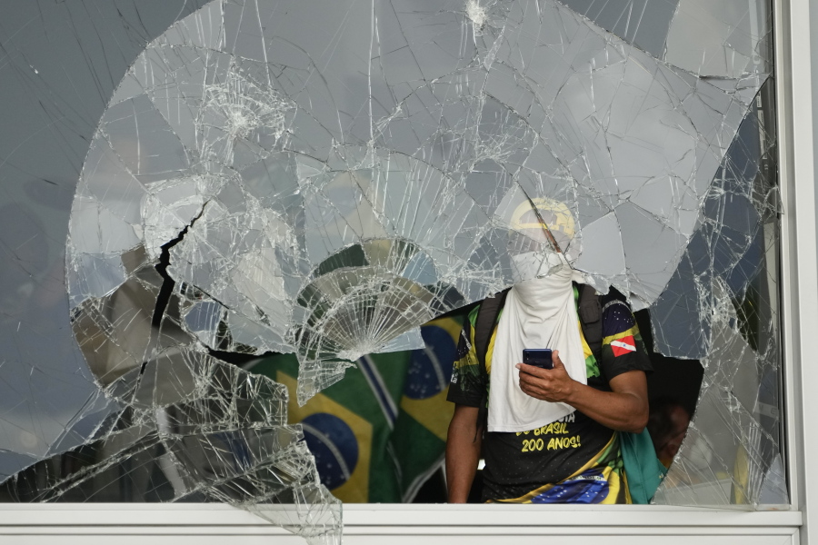 Protesters, supporters of Brazil's former President Jair Bolsonaro, look pout from a shattered window after they storm the Planalto Palace in Brasilia, Brazil, Sunday, Jan. 8, 2023. Planalto is the official workplace of the president of Brazil.
