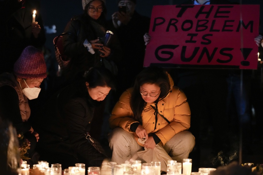 Women place candles at a memorial while a man holds a sign during a vigil outside Monterey Park City Hall, blocks from the Star Ballroom Dance Studio on Tuesday, Jan. 24, 2023, in Monterey Park, Calif. A gunman killed multiple people at the ballroom dance studio late Saturday amid Lunar New Years celebrations in the predominantly Asian American community.