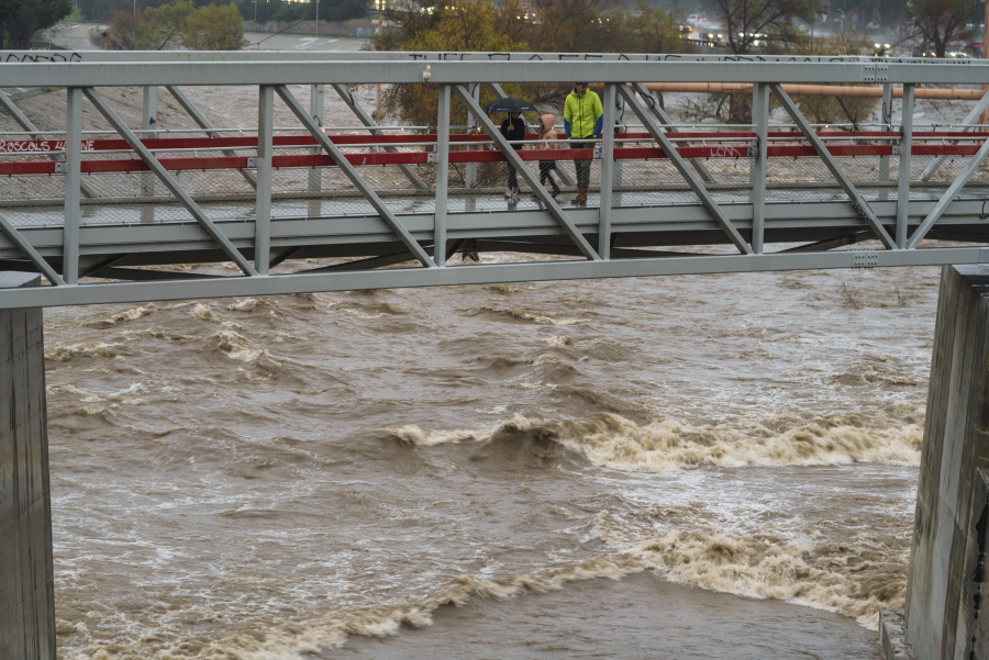 People cross a bridge over a swollen Los Angeles River in Los Angeles on Saturday, Jan. 14, 2023. Storm-battered California got more wind, rain and snow on Saturday, raising flooding concerns, causing power outages and making travel dangerous.