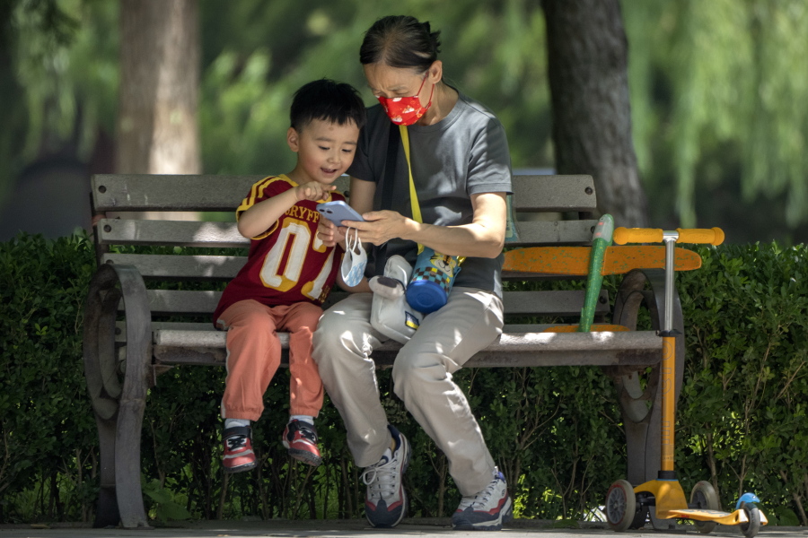 FILE - A woman wearing a face mask and a child look at a cellphone as they sit on a bench at a public park in Beijing, on June 2, 2022. As the week-long Lunar New Year holidays in China draw near with promises of feasts and red envelopes stuffed with cash, children have yet another thing to look forward to - one extra hour of online games each day.