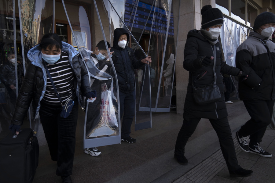 Travelers wearing face masks walk out of an exit of the Beijing Railway Station in Beijing, Saturday, Jan. 14, 2023. Millions of Chinese are expected to travel during the Lunar New Year holiday period this year.