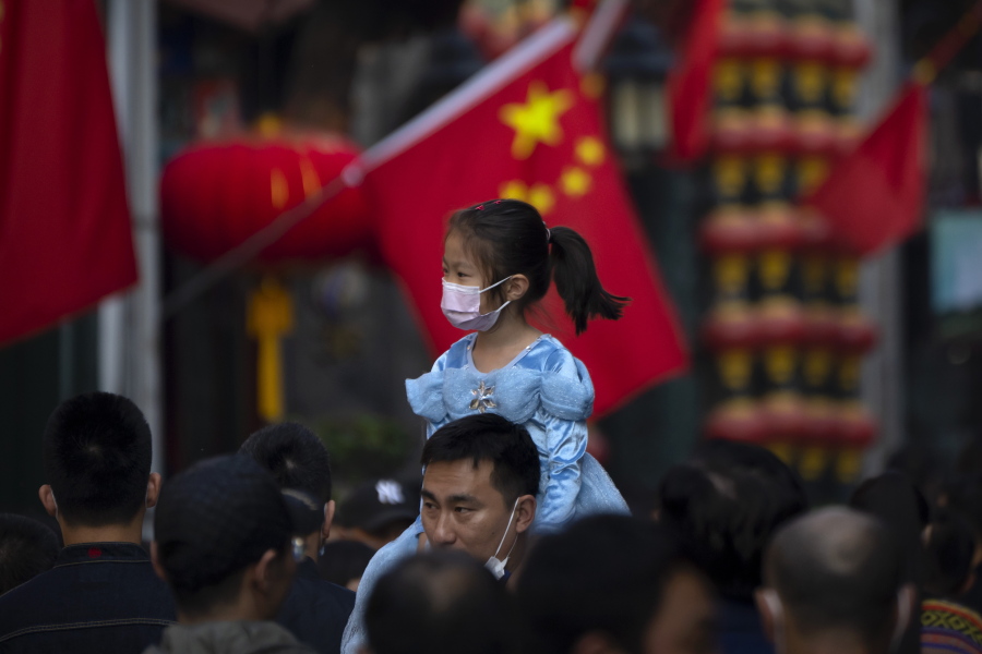 FILE - A girl wearing a face mask rides on a man's shoulders as they walk along a tourist shopping street in Beijing on Oct. 7, 2022. China has announced its first overall population decline in recent years amid an aging society and plunging birthrate.