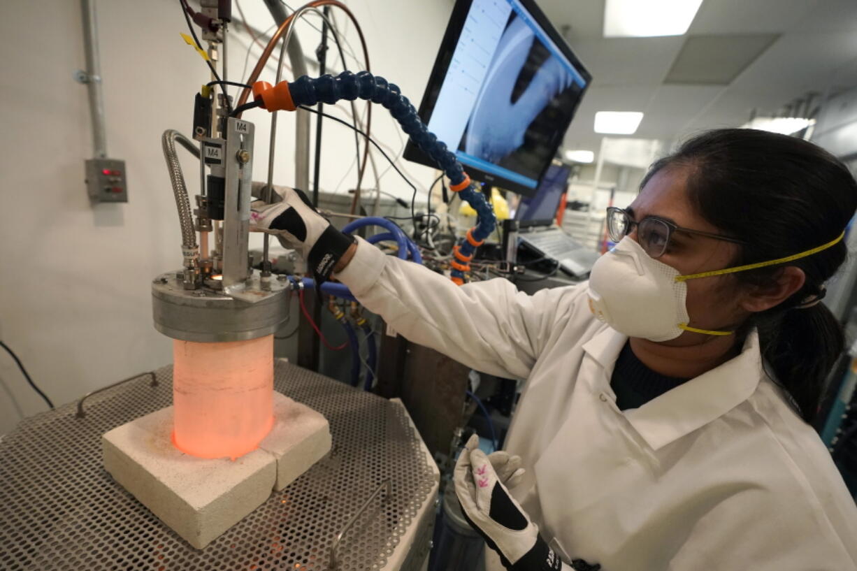 Research and development engineer Ravneet Kailey performs an experiment to produce steel without using carbon in a glowing lab cell, left, Wednesday, Jan. 25, 2023, at Boston Metal, in Woburn, Mass. The manufacture of 'green steel' moved one step closer to reality Friday, Jan. 27, as Boston Metal announced a $120 million investment from the world's second-largest steelmaker, ArcelorMittal.