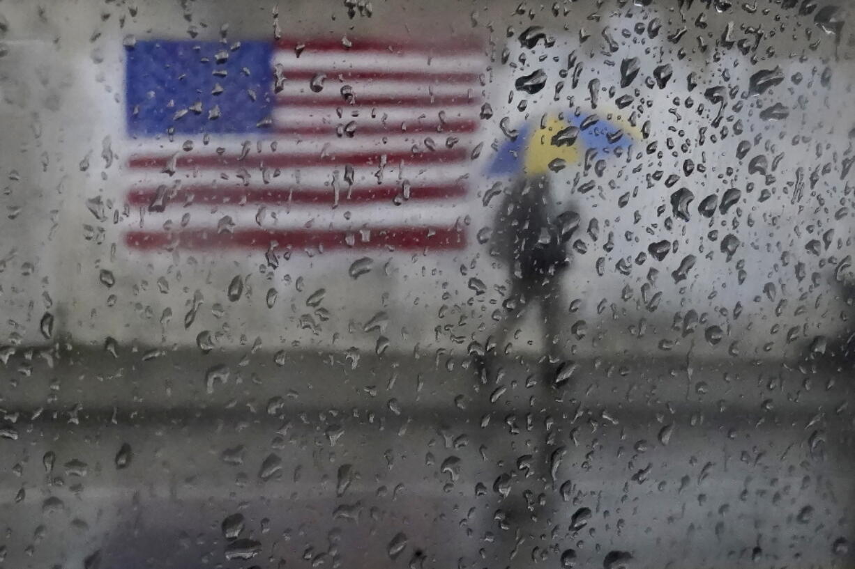 FILE - A pedestrian carries an umbrella while walking past a painting of an American flag in San Francisco, Jan. 11, 2023. A new study says the drenching that California has been getting since Christmas will only get wetter and nastier with climate change.