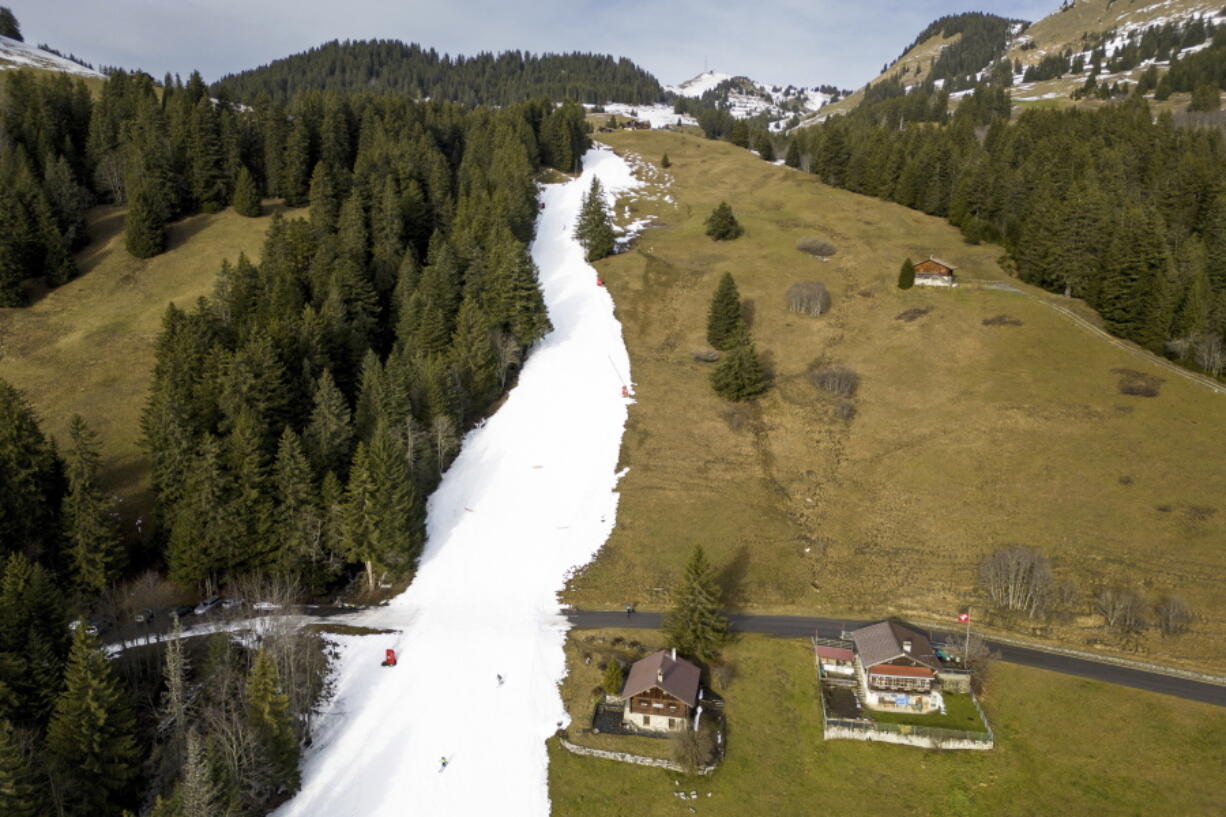 Skiers speed down a ski slope with artificial snow in the middle of a snowless field, at 1600 meters above sea level, in the alpine resort of Villars-sur-Ollon, Switzerland, Saturday, Dec. 31, 2022. Sparse snowfall and unseasonably warm weather in much of Europe is allowing green grass to blanket many mountaintops across the region where snow might normally be. It has caused headaches for ski slope operators and aficionados of Alpine white this time of year.