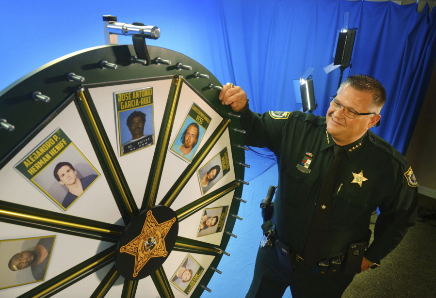 FILE - Brevard County Sheriff Wayne Ivey gets ready to spin his popular "Wheel of Fugitive" in July 2017, in Titusville, Fla. A man has filed a defamation lawsuit last week against Ivey who posts weekly "Wheel of Fugitive" videos on social media.