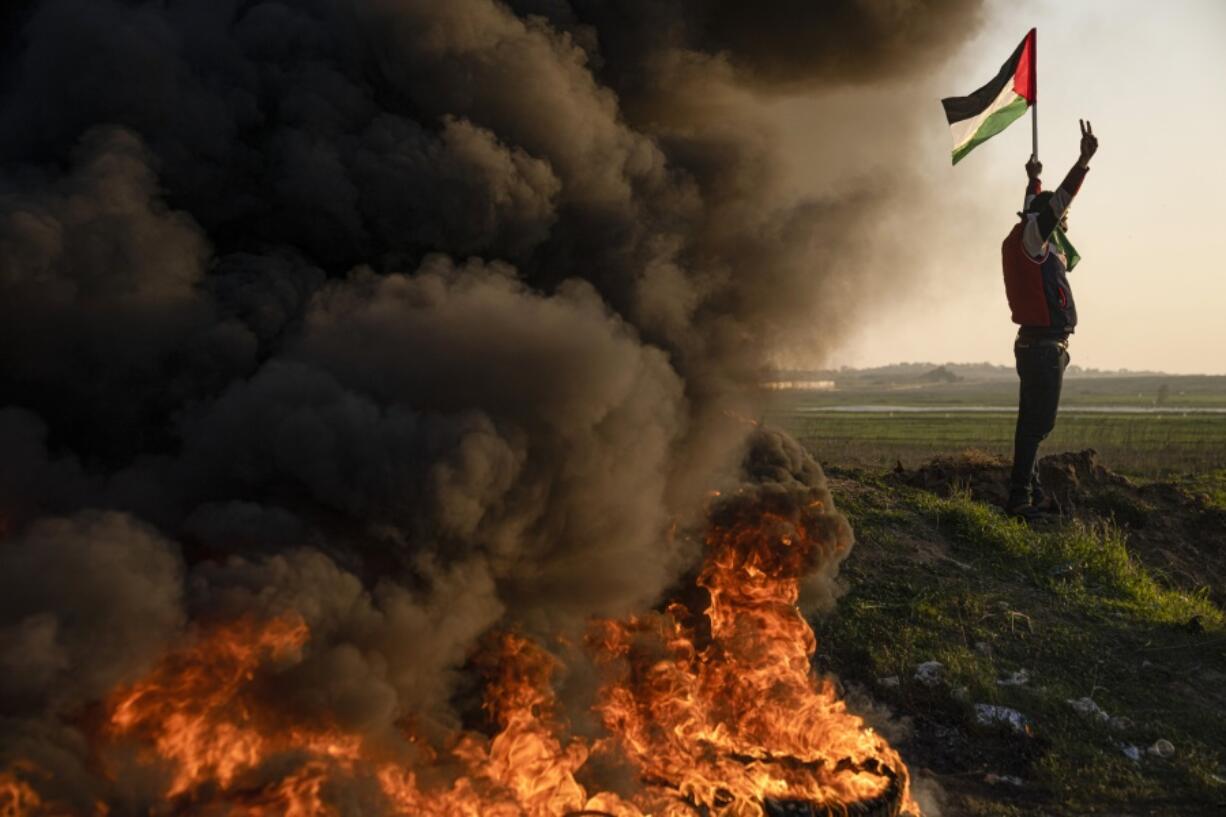 Palestinians burn tires and wave the national flag during a protest against Israeli military raid in the West Bank city of Jenin, along the border fence with Israel, in east of Gaza City, Thursday, Jan. 26, 2023. During the raid in the West Bank town of Jenin, Israeli forces killed at least nine Palestinians, including a 60-year-old woman, and wounded several others, Palestinian health officials said, in one of the deadliest days of fighting in years. The Israeli military said it was conducting an operation to arrest militants when a gun battle erupted.